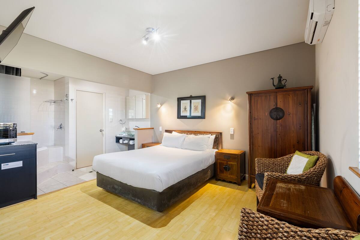 A modern bedroom with a large bed, bedside tables, a wardrobe, and a wicker chair.