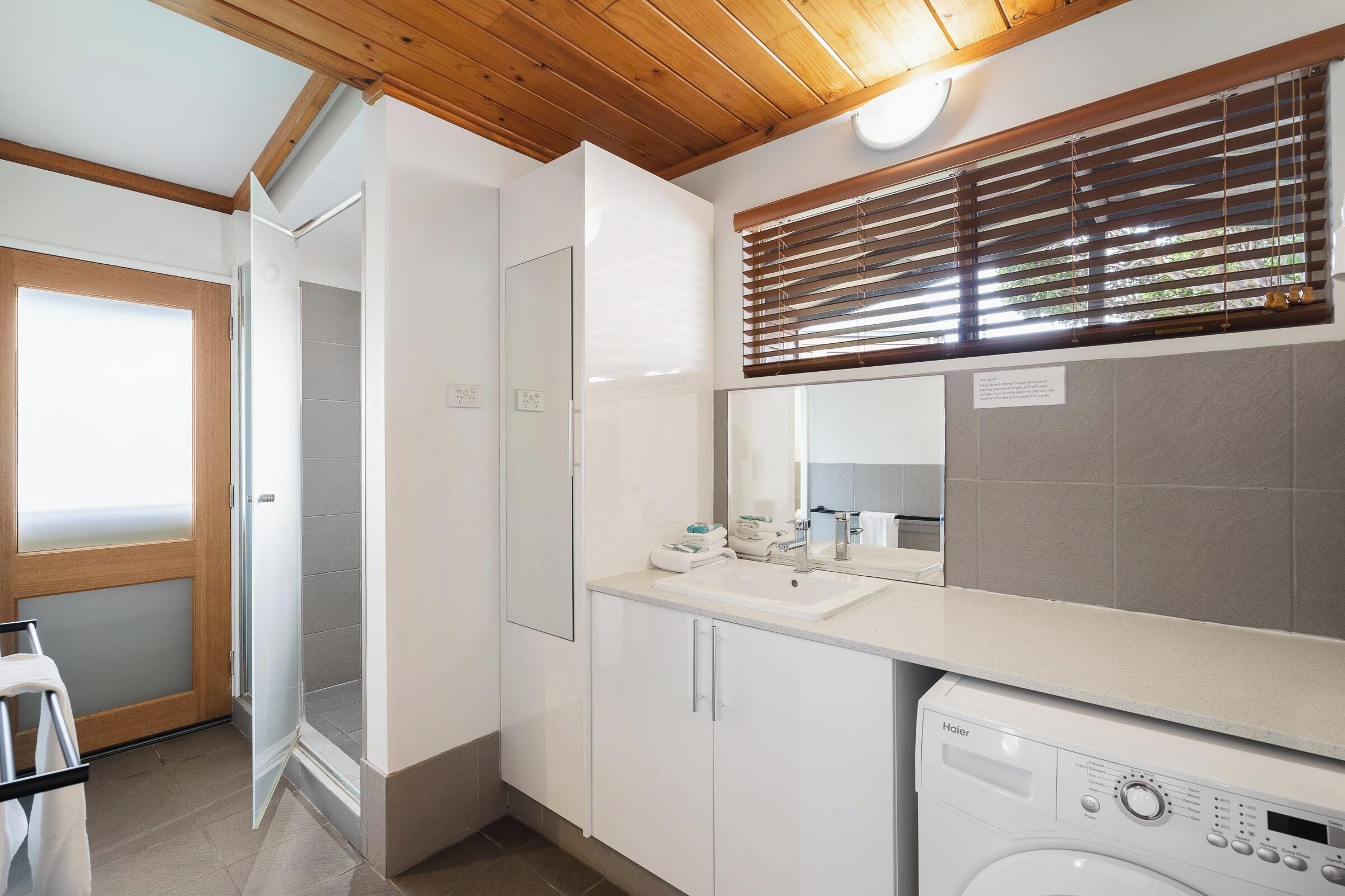 A modern bathroom with a built-in washing machine, a large mirror, and a shower area.