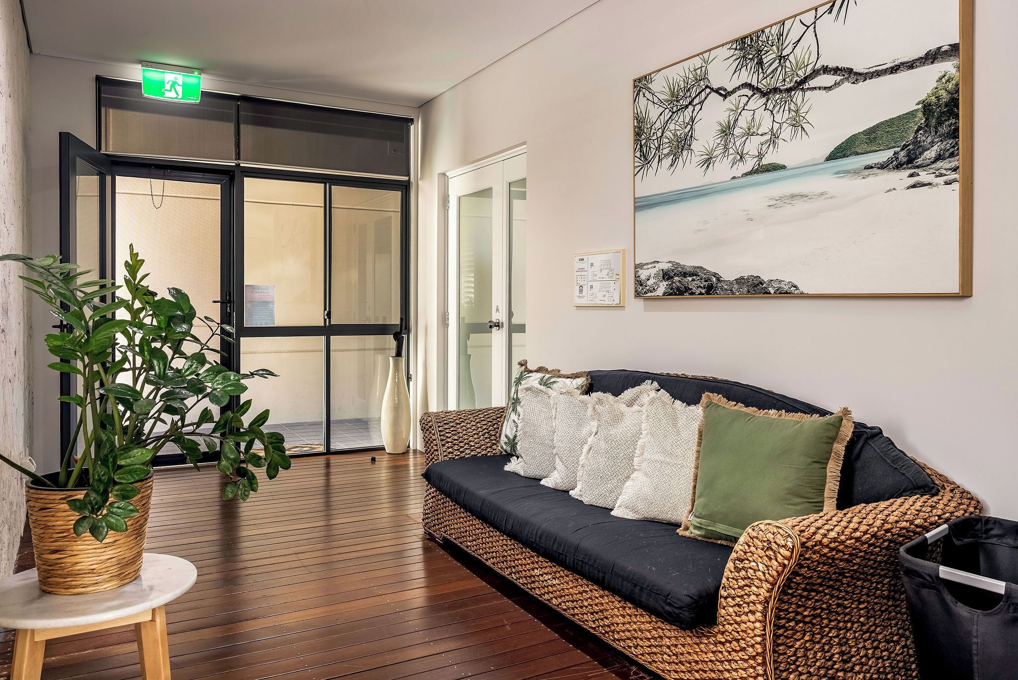 A lobby with a woven sofa, a potted plant, and a painting of a beach scene.