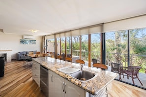 A modern kitchen with a granite countertop, stainless steel sink, and wooden flooring. - Bay Village Resort Dunsborough (Dunsborough)