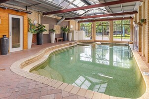 Una piscina interior con borde de ladrillo, plantas grandes en macetas y una puerta de madera.