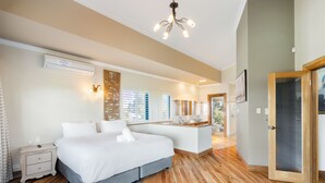 A modern bedroom with a large bed, wooden flooring, a built-in desk, and a bathroom visible through an open door. - Bay Village Resort Dunsborough (Dunsborough)