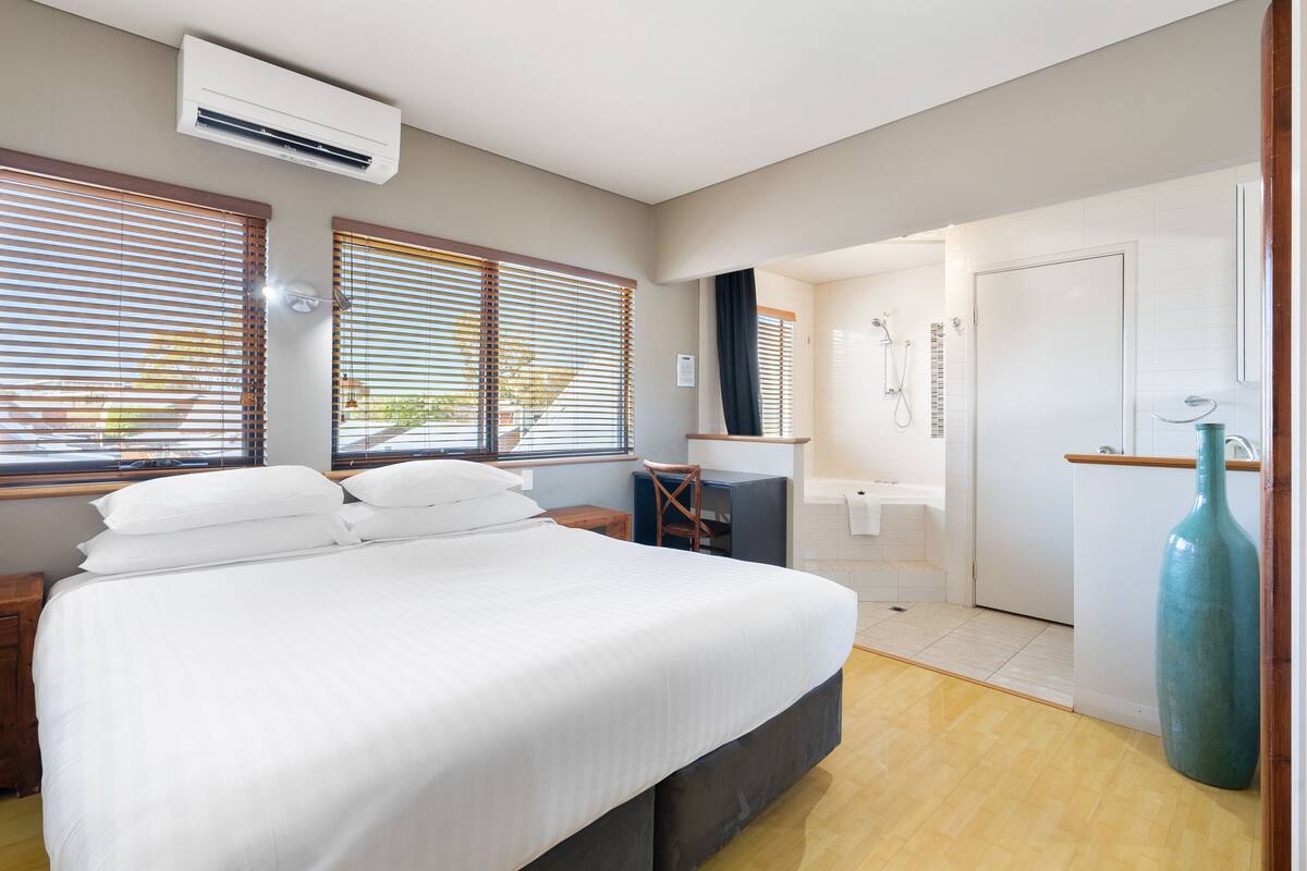 A bedroom with a bed, a desk, a chair, a large vase, and a bathroom with a shower and toilet.