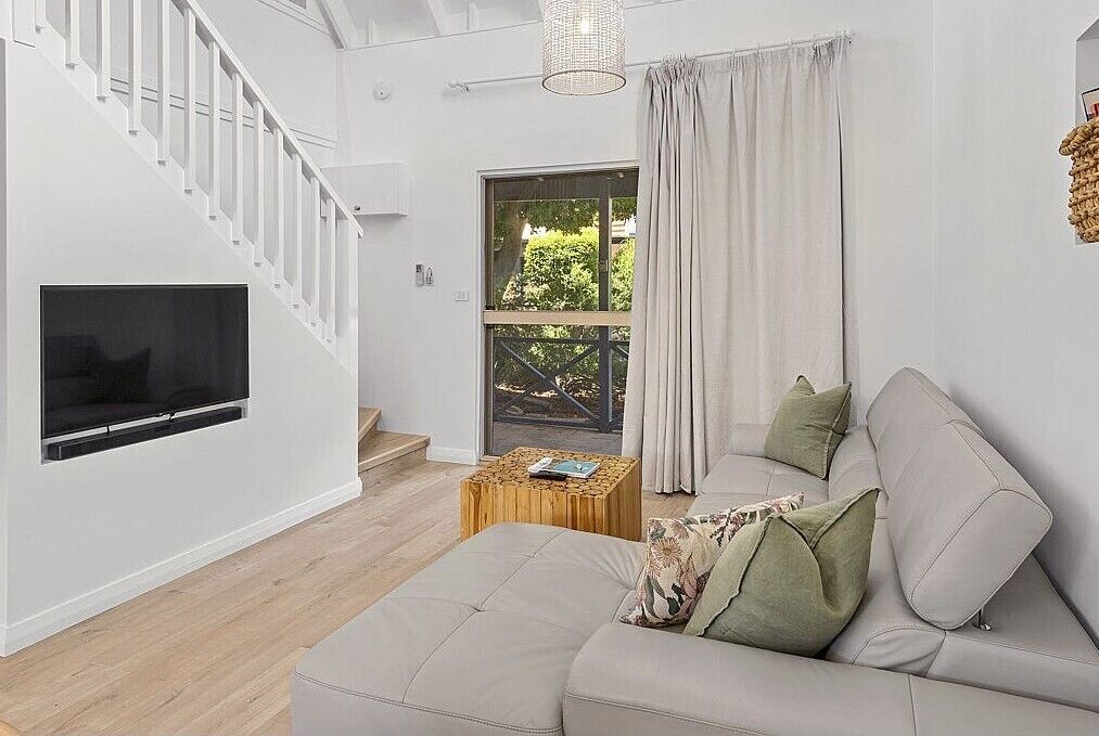 A modern living room with a sofa, a TV, a wooden coffee table, and a staircase.