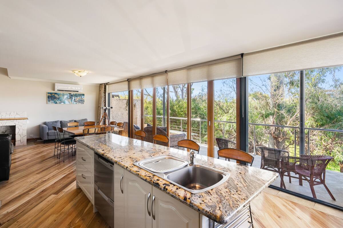 A modern kitchen with a granite countertop, stainless steel sink, and wooden flooring.