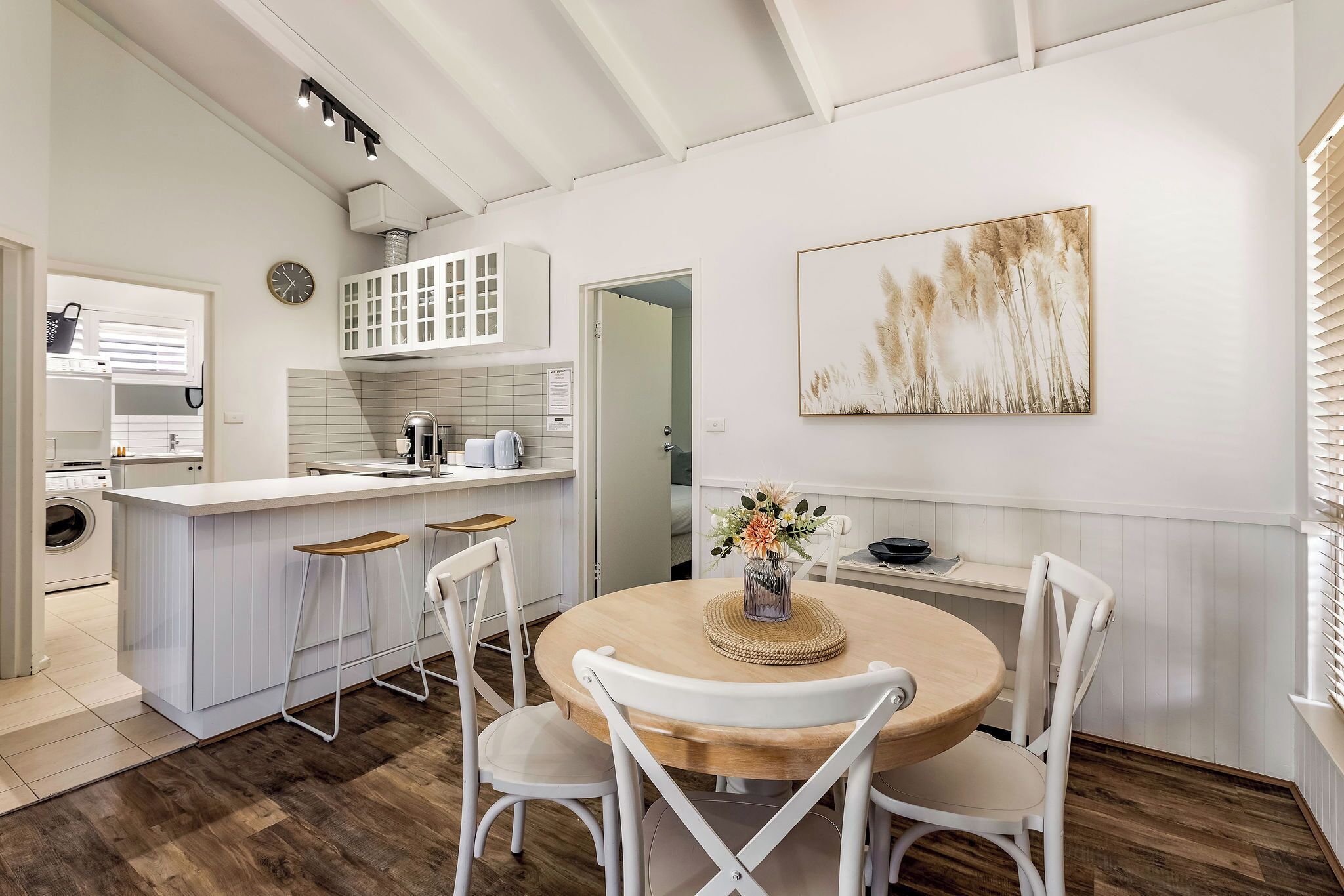 Une cuisine moderne avec des meubles blancs, un îlot central en bois et un coin repas avec des chaises blanches.