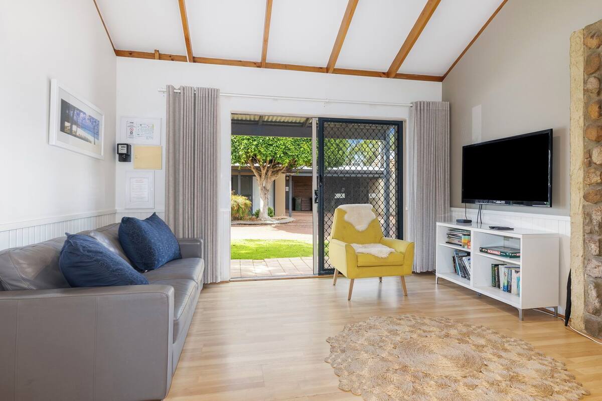 A modern living room with a grey sofa, a yellow armchair, a flat-screen TV, and a bookshelf.