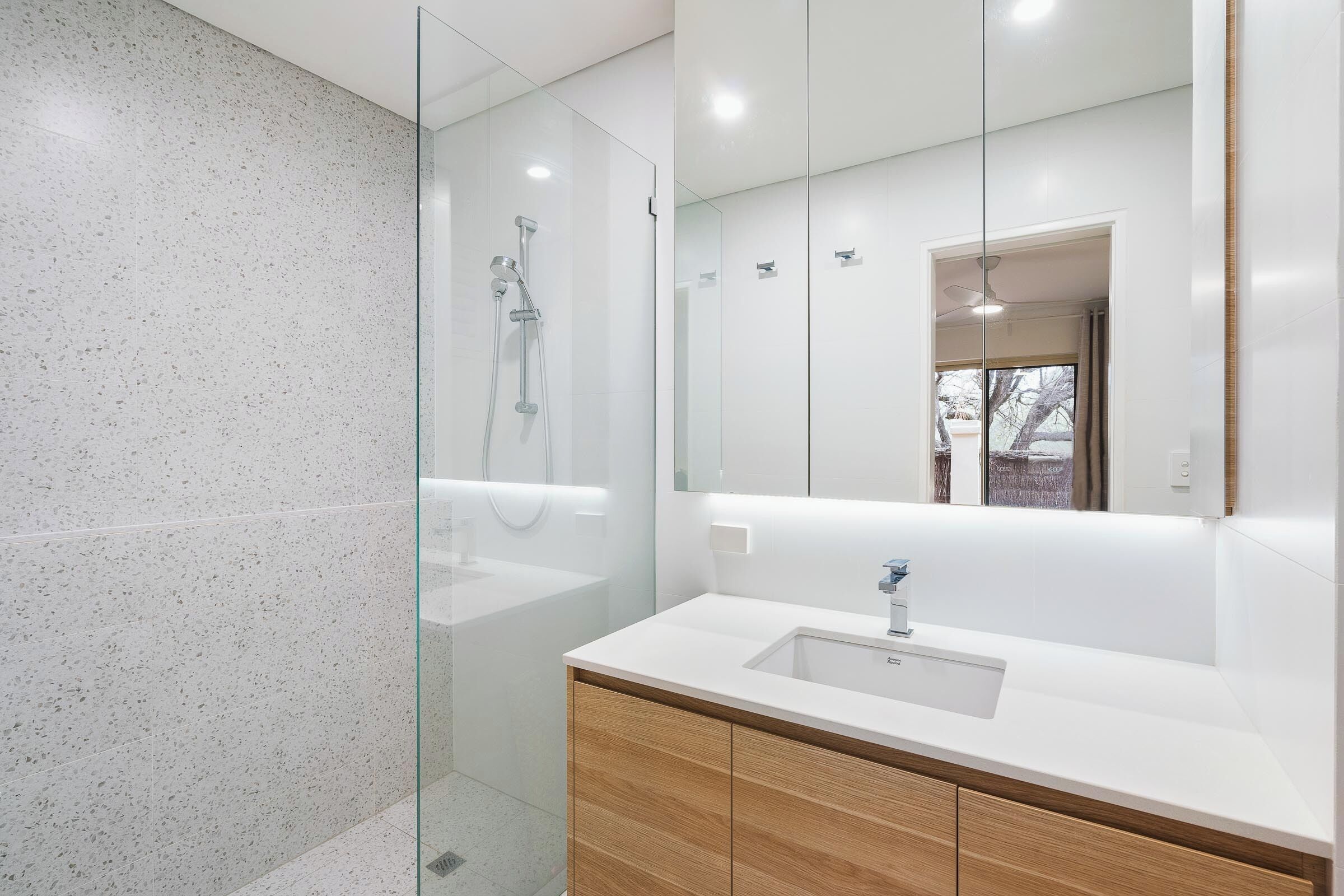 A modern bathroom with a glass shower enclosure, a white sink, wooden cabinets, and a large mirror.