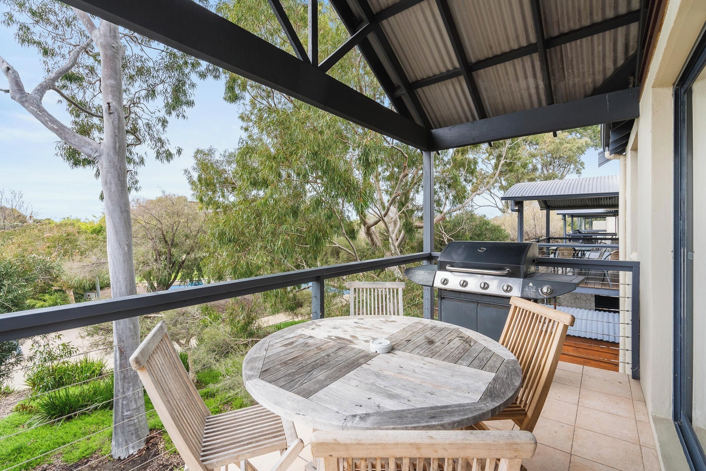 An outdoor patio with a round wooden table and chairs, a grill, and a view of the surrounding landscape.