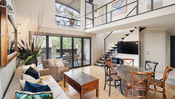A spacious living area with a sofa, coffee table, and dining set. A staircase leads to an upper level with a balcony. - Bay Village Resort Dunsborough (Dunsborough)