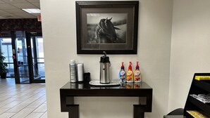A reception desk with a framed horse portrait, a coffee station with branded bottles, and a piano in the background. - Budget Inn (Laramie)