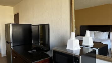 Una camera d'albergo con un minibar, una TV a schermo piatto, un forno a microonde e un letto con biancheria bianca.