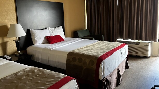 A hotel room with two beds, a large headboard, a desk with a lamp, a chair, and a window with curtains. - Budget Inn (Laramie)