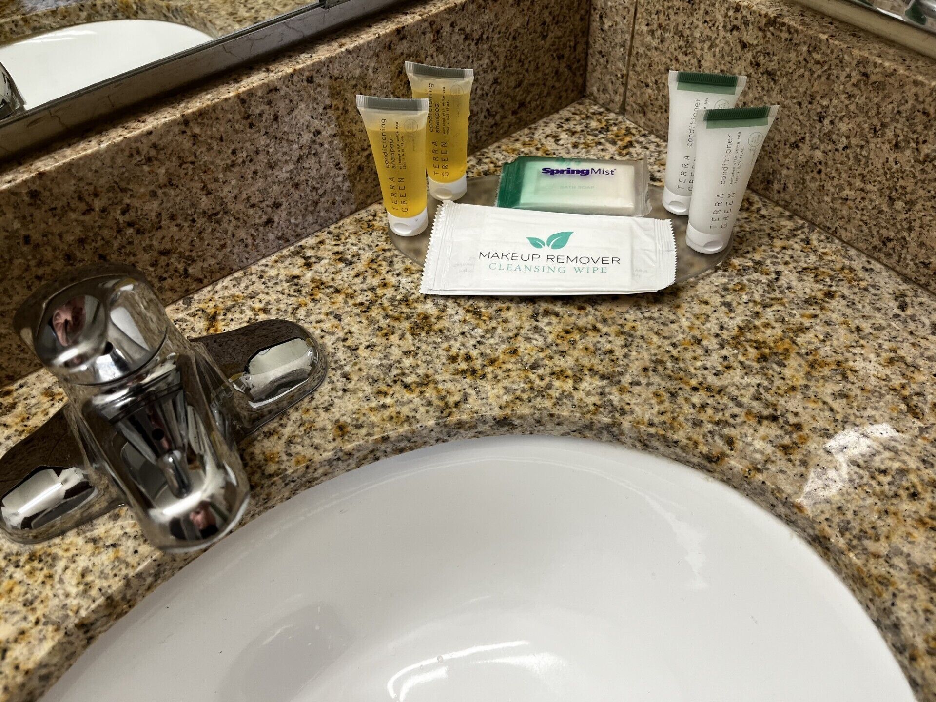 Un lavamanos de baño con artículos de aseo, incluyendo toallitas desmaquillantes, una pastilla de jabón y dos botellas de champú.