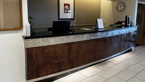 A hotel reception desk with a black counter, a framed picture on the wall, a clock, and a sign with information. - Budget Inn (Laramie)