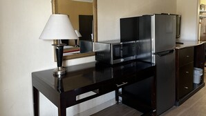 A compact kitchenette with a microwave, refrigerator, and a small table with a lamp. - Budget Inn (Laramie)