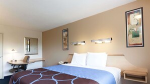 Habitación de hotel con cama, escritorio, silla, teléfono e iluminación en la pared.