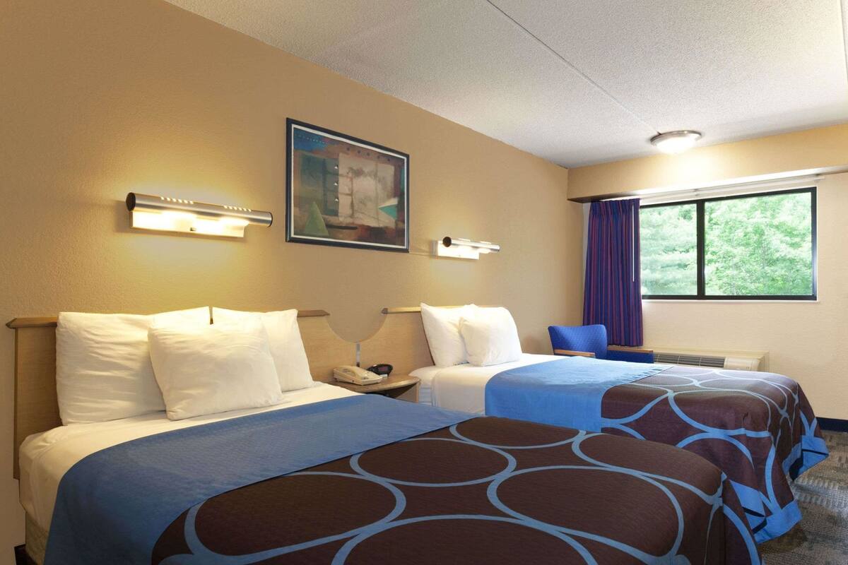 A hotel room with two beds, a nightstand, a telephone, a painting on the wall, and a window with curtains.