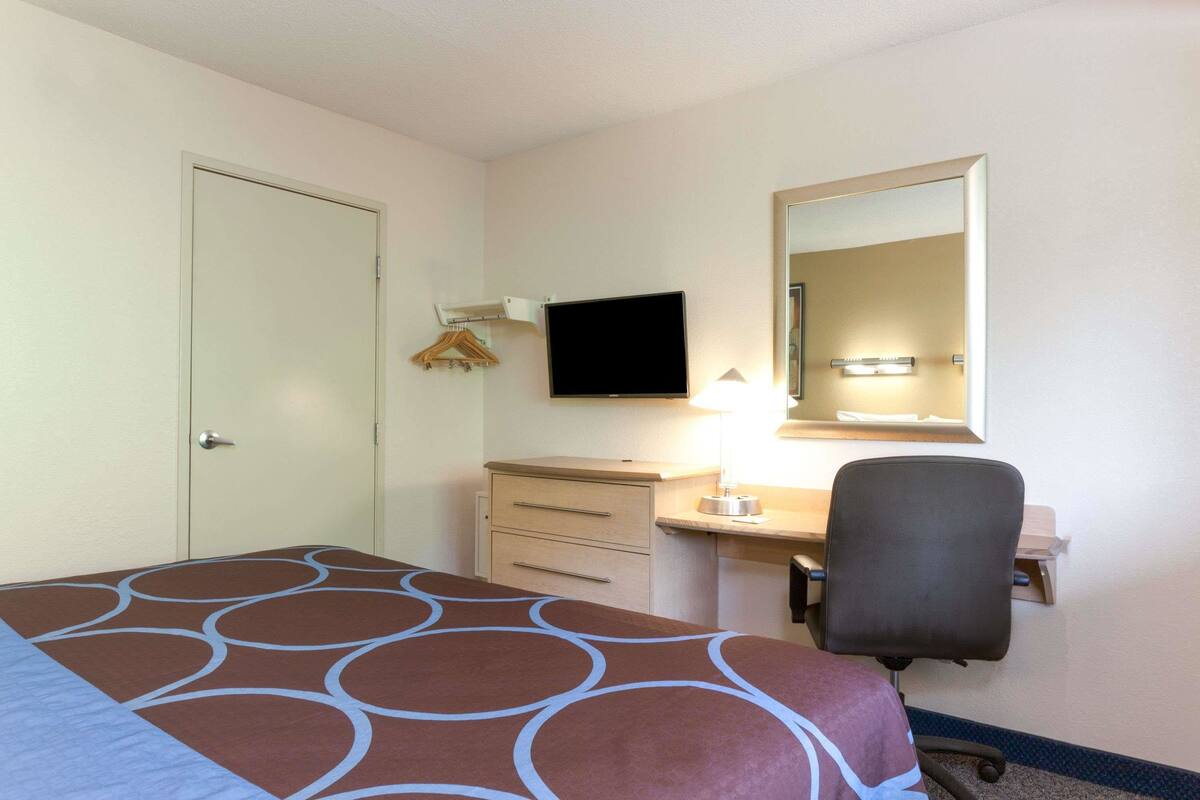A hotel room with a bed, a desk with a computer, a chair, a TV, and a mirror.
