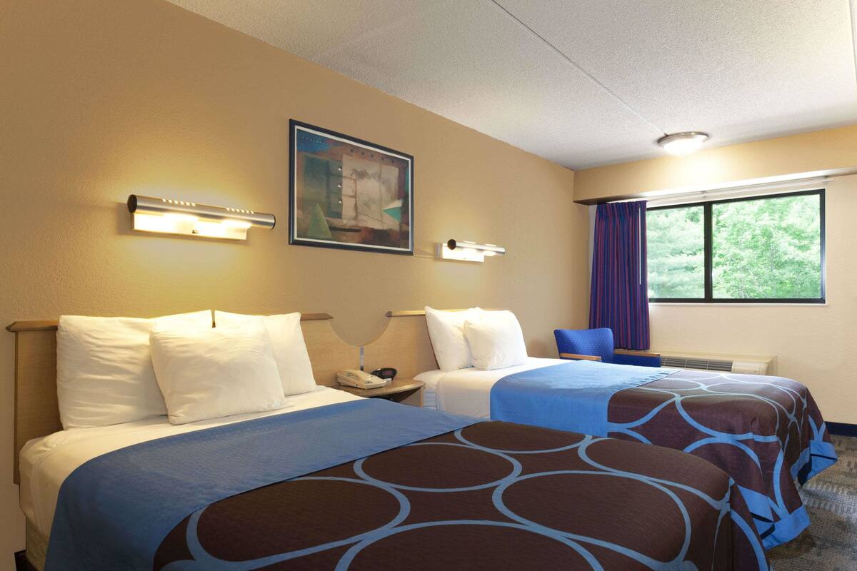 A hotel room with two beds, a nightstand, a painting, and a window with curtains.