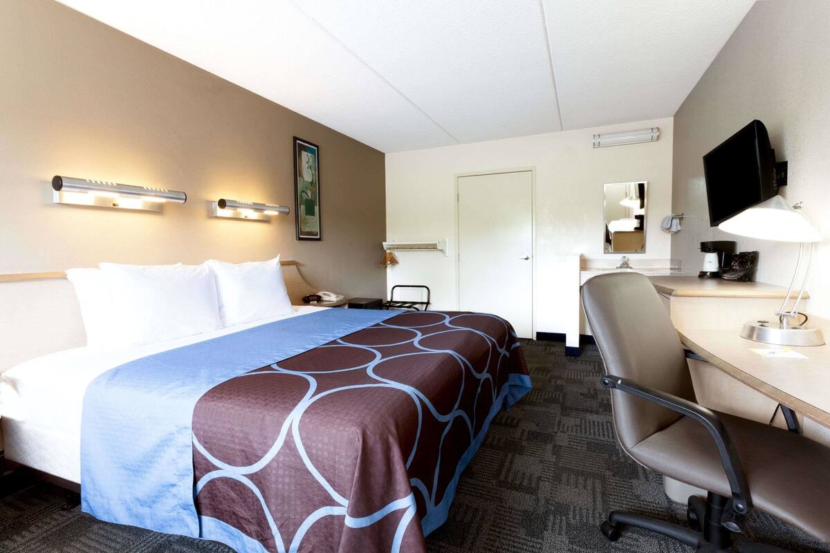 A hotel room with a bed, a desk, a chair, a television, and a mirror.