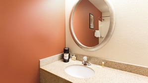 Un baño con un espejo redondo, un lavabo y una cafetera sobre la encimera.