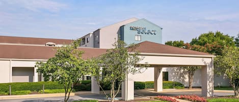 A hotel with a modern design, featuring a covered parking area and a landscaped garden with red flowers.