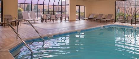 Una piscina interior con agua cristalina, rodeada de sillones de descanso y una zona de patio con paredes de vidrio.