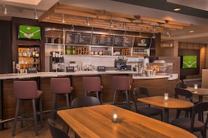 A bar area with a wooden counter, bar stools, and tables. There are menu boards above the counter and a television screen on the wall.