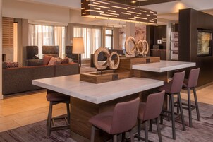 Un moderno vestíbulo de hotel con una zona de bar central, asientos y una recepción.