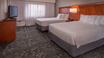 A hotel room with two beds, a TV, a desk, and a window with curtains.