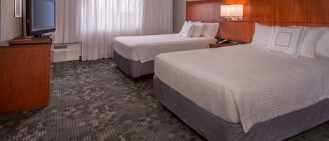 A hotel room with two beds, a TV, a desk, and a window with curtains.