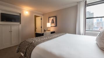 Una habitación de hotel con cama, televisor montado en la pared, mesita de noche con lámpara y ventana con vista a la ciudad.