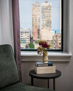 Enjoy the city view from this stylish room, featuring a comfortable chair and a small table with a vase and a book.
