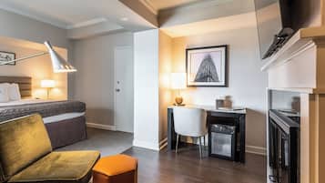 A hotel room with a bed, a desk, a chair, a lamp, and a fireplace.