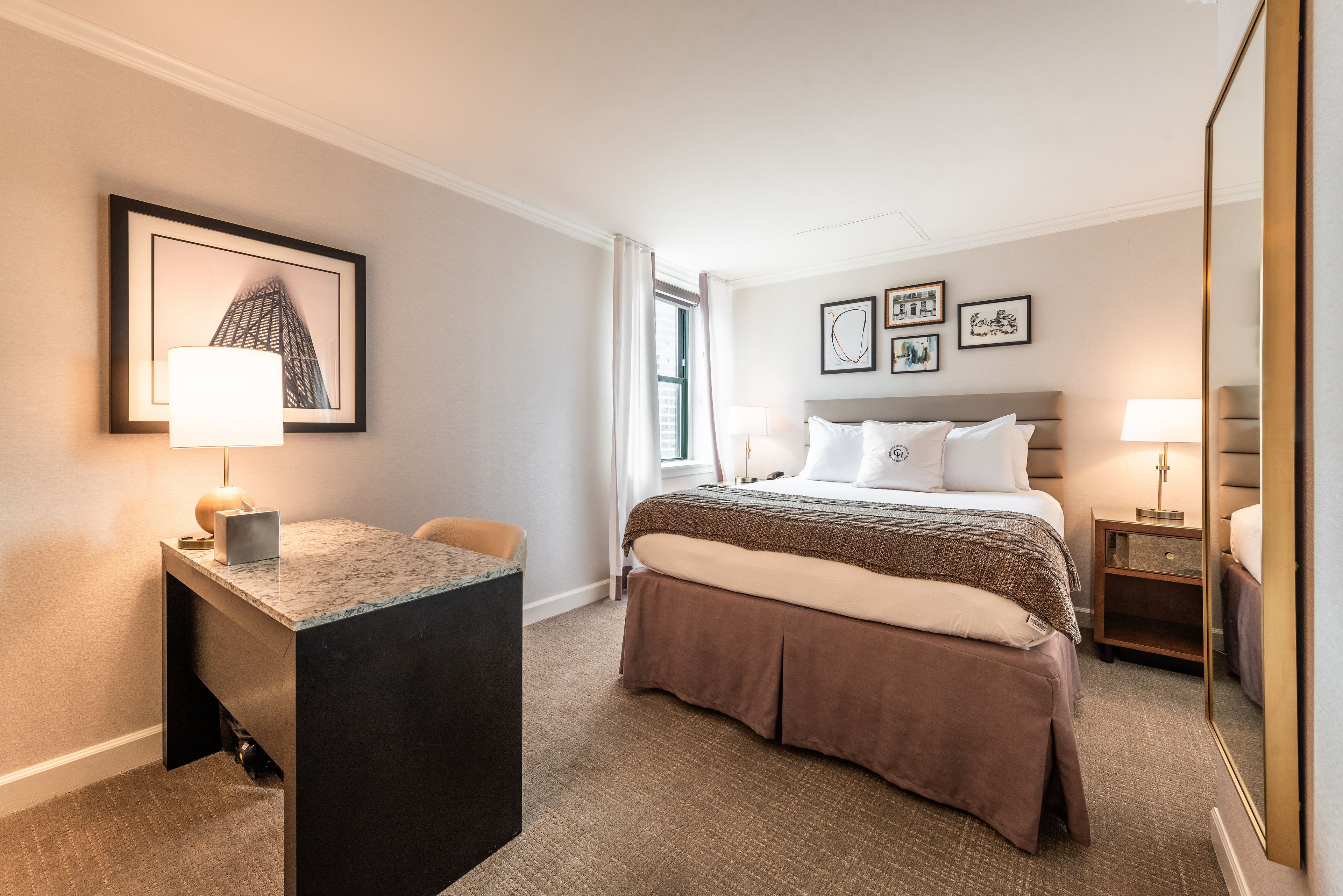 Quarto de hotel com cama, escrivaninha, cadeira, espelho e obras de arte nas paredes.