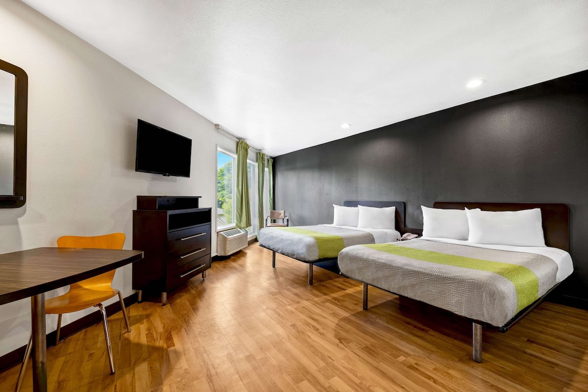 A hotel room with two beds, a desk, a chair, a TV, and a window with curtains.