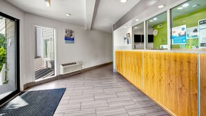 A reception area with a wooden reception desk, a glass partition, and a view of the outdoors. - Studio 6 Portland, OR (Portland)