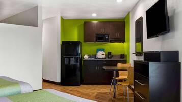 A compact hotel room with a kitchenette, a bed, a desk, and a TV.