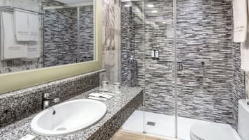 A modern bathroom with a granite countertop, a white sink, a glass shower enclosure, and a toilet.