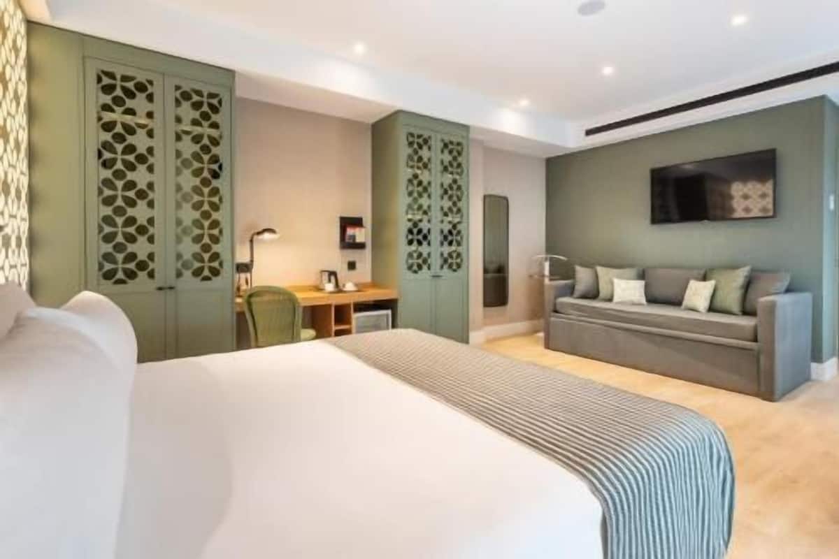 Quarto de hotel com uma cama grande, uma escrivaninha, um sofá e uma televisão.