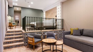 Una sala de estar moderna con un sofá, dos sillones, una mesita de centro y una escalera con azulejos estampados.