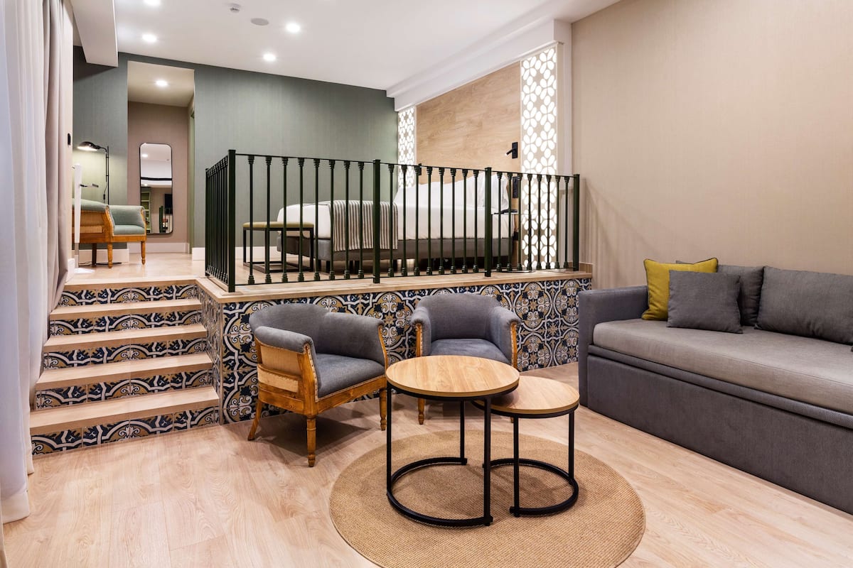 Uma sala de estar moderna com um sofá, duas poltronas, uma mesa de centro e uma escada com ladrilhos estampados.