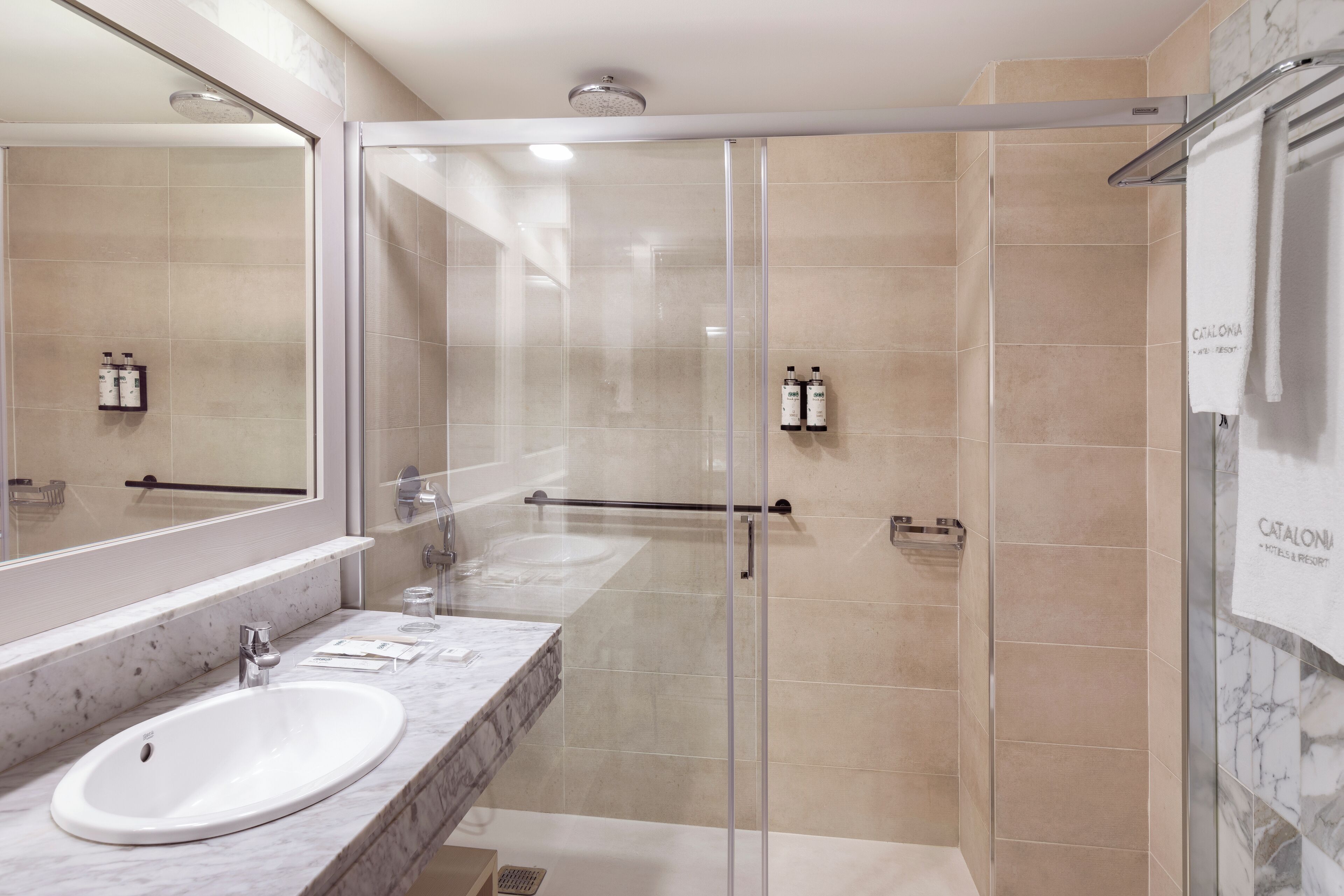 Ein modernes Badezimmer mit einer gläsernen Dusche, einem großen Spiegel und einer Marmorarbeitsplatte.