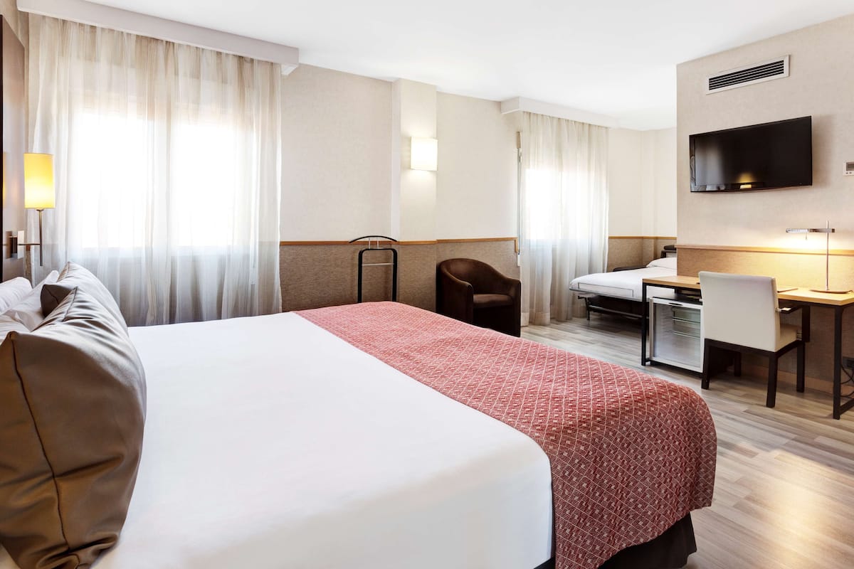 Quarto de hotel com uma cama grande, uma escrivaninha, uma cadeira, televisão e banheiro.