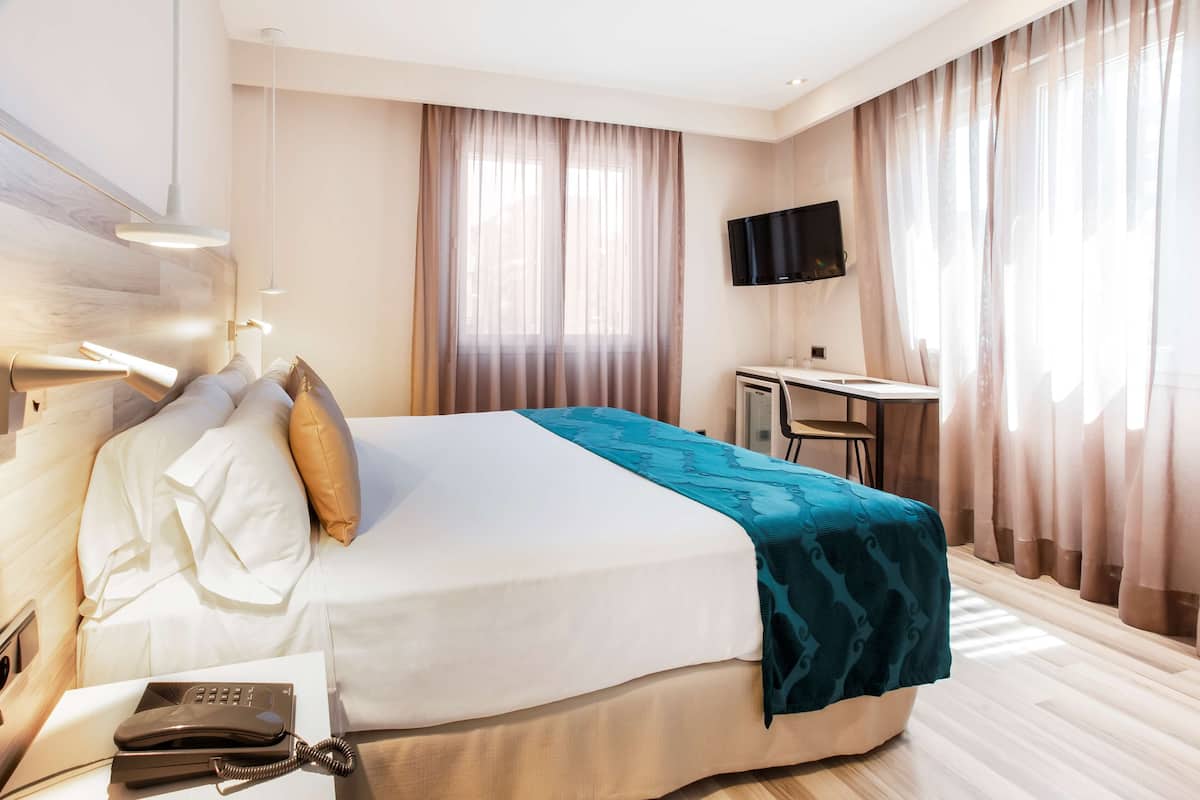 Quarto de hotel com cama, escrivaninha, televisão e telefone.