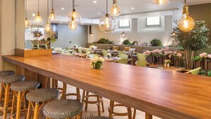 Un restaurante con una barra de madera larga, sillas de mimbre y lámparas colgantes.
