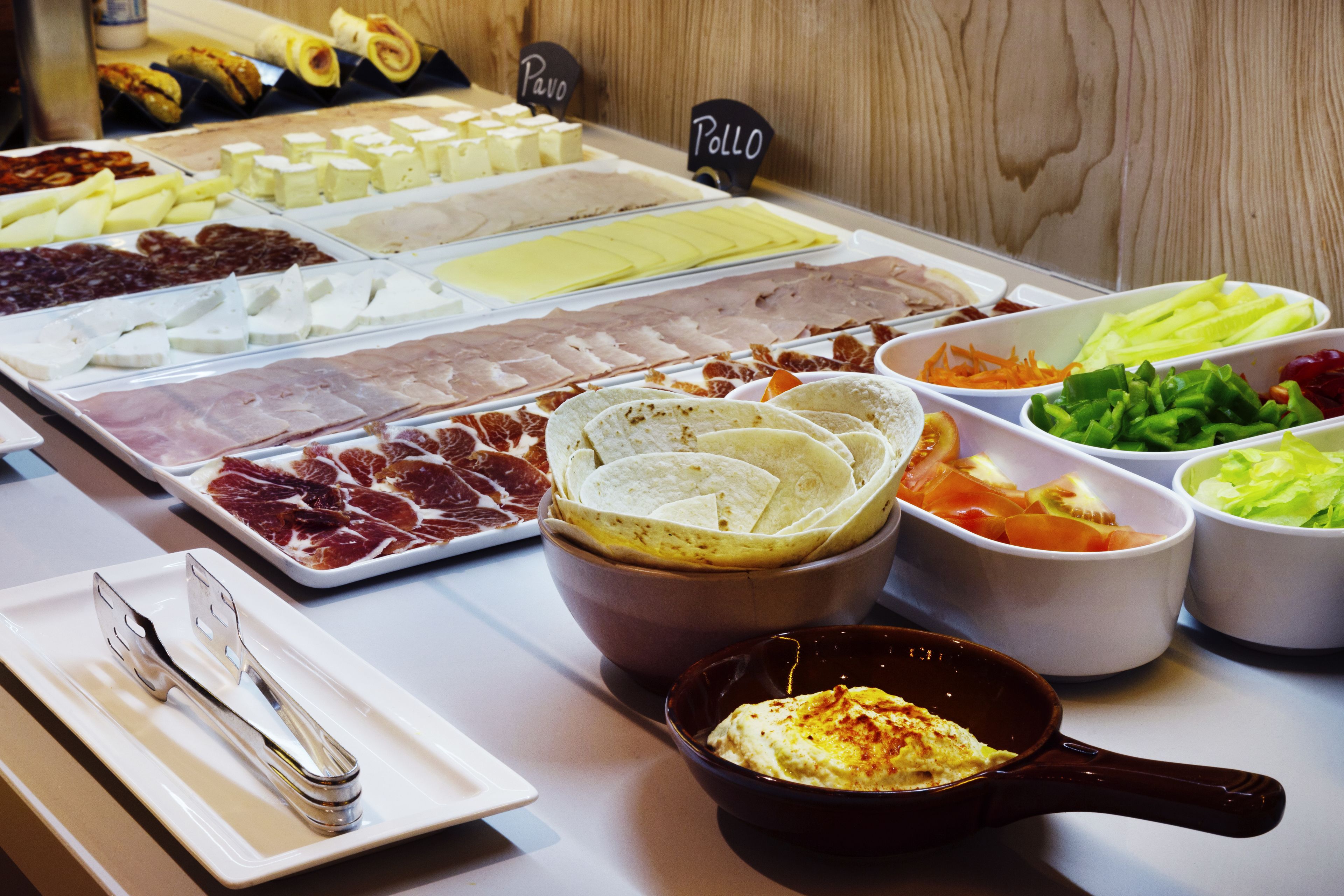 Un bufé con diversas opciones de comida, incluyendo carnes, quesos y verduras.
