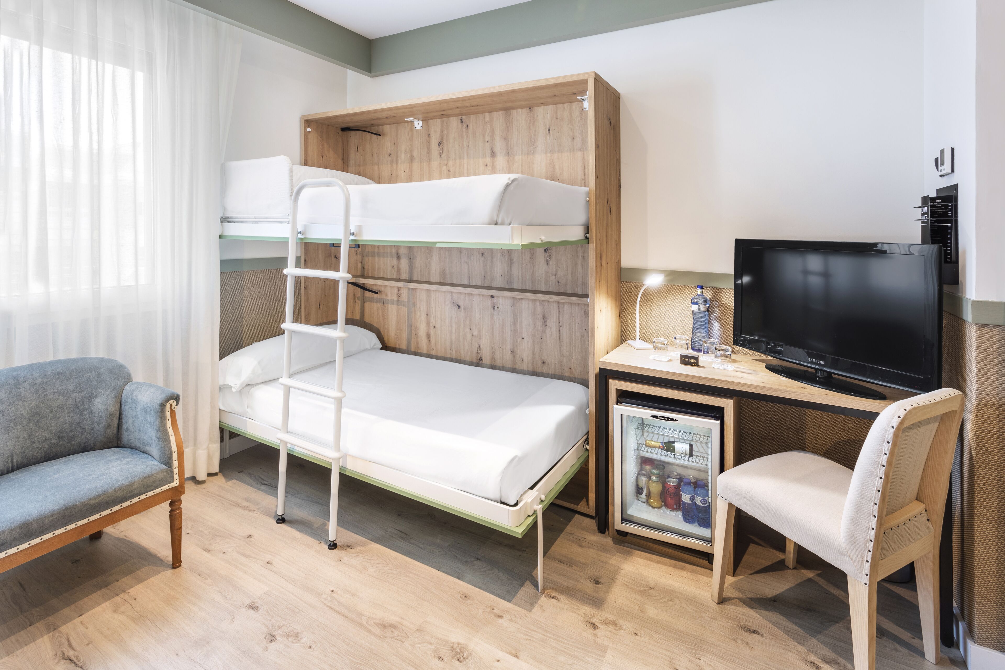 Una cama litera con escalera, un escritorio con televisor, una silla y un refrigerador pequeño.