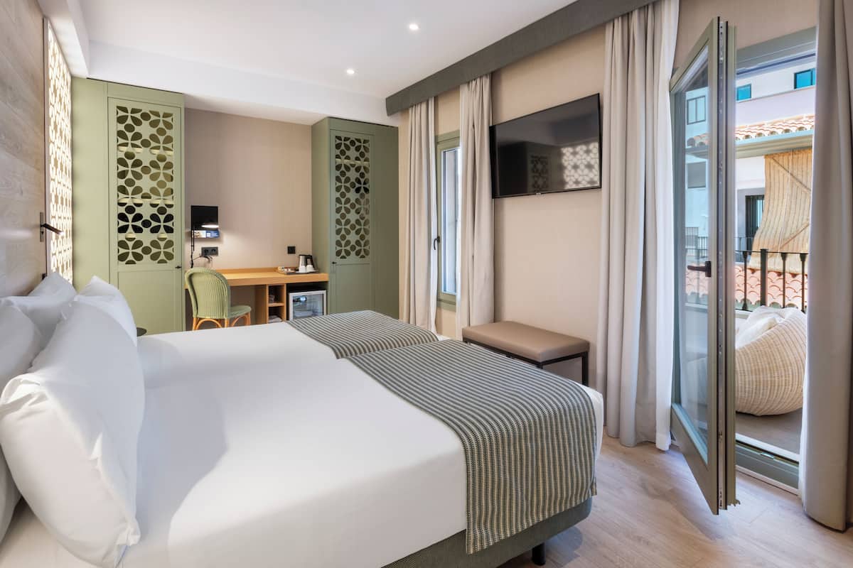 Quarto de hotel com duas camas, uma escrivaninha, televisão e varanda com vista.